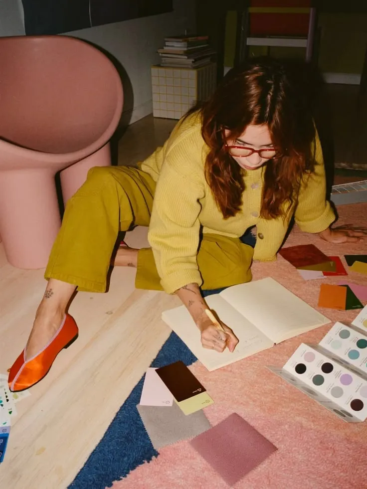 A designer lying on the floor writing in a notebook among colour swatches